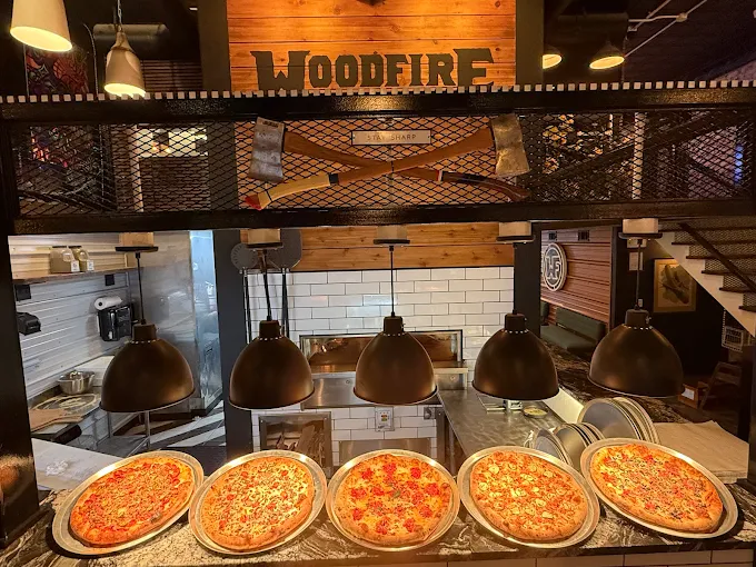 Woodfire Pizza Kitchen Image of pizzas under a warmer with the woodfire oven in the background.